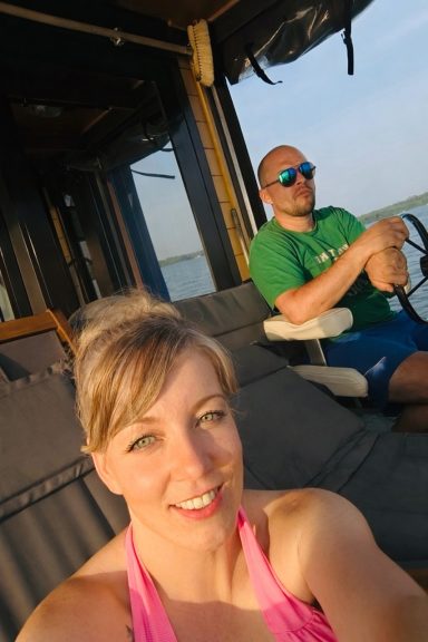 Eine Frau in einem pinken Outfit und ein Mann in Sonnenbrille sitzen auf einem Boot.