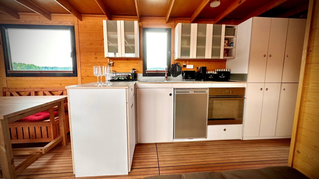 Moderne Küche mit Holzdetails, weißen Schränken und großen Fenstern.