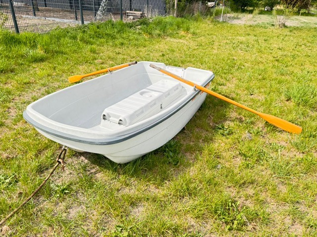 Ein graues Boot mit einem weißen Kasten und einem orangefarbenen Paddel auf Gras.