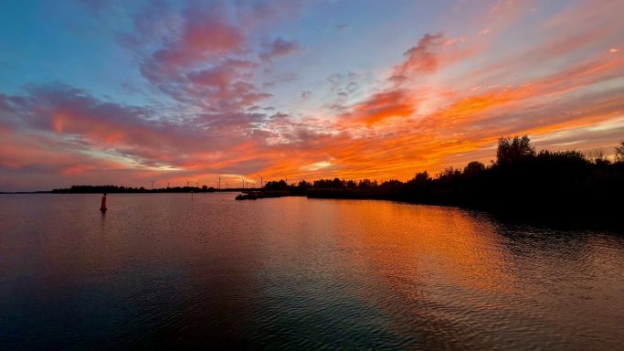 Sonnenuntergang über ruhigem Wasser mit lebhaften orangefarbenen und blauen Wolken.