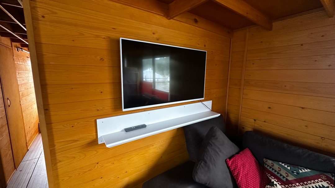 Fernseher an der Wand über einem weißen Regal in einem Holzzimmer.