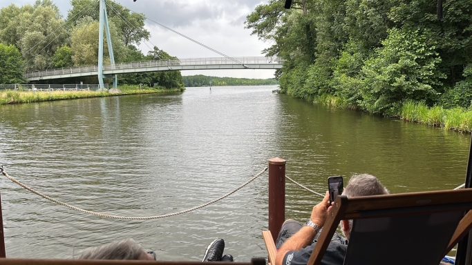 Blick auf einen ruhigen Fluss mit einer Brücke und üppiger Vegetation am Ufer.