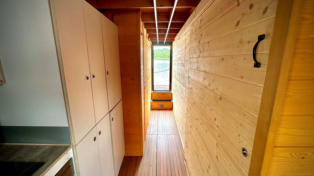 Blick auf einen schmalen Flur mit Holzverkleidung und Küchenschränken an der Seite.