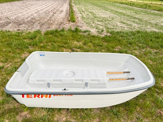 Ein leeres, weißes Boot mit zwei Rudern auf grünem Gras vor einem Feld.