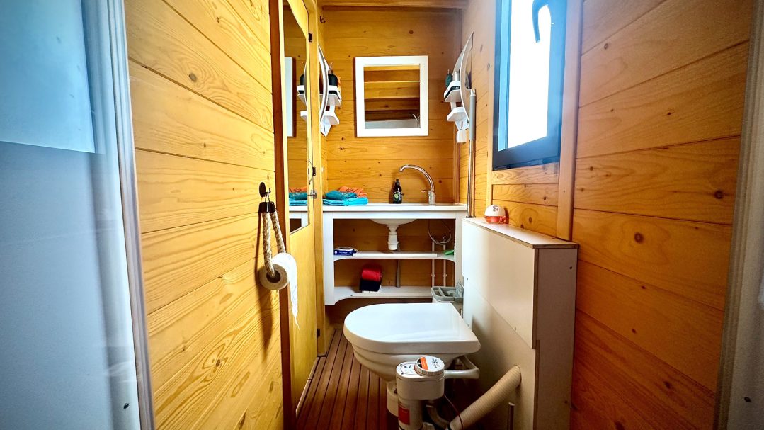 Kleines Badezimmer mit Holzwänden, Toilette, Waschbecken und Spiegel.