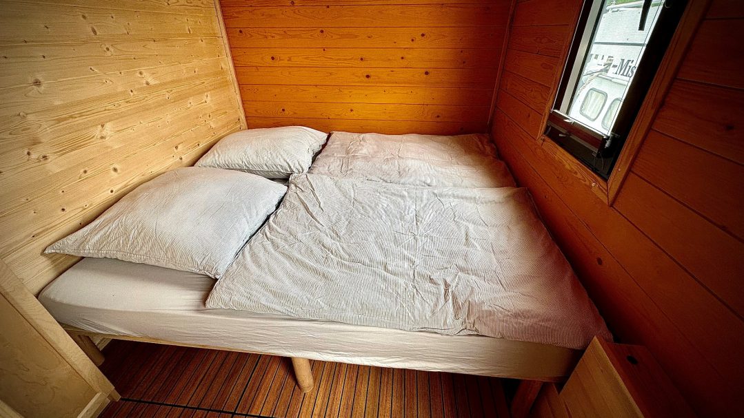 Ein einfaches Bett im Innenraum einer hölzernen Unterkunft.